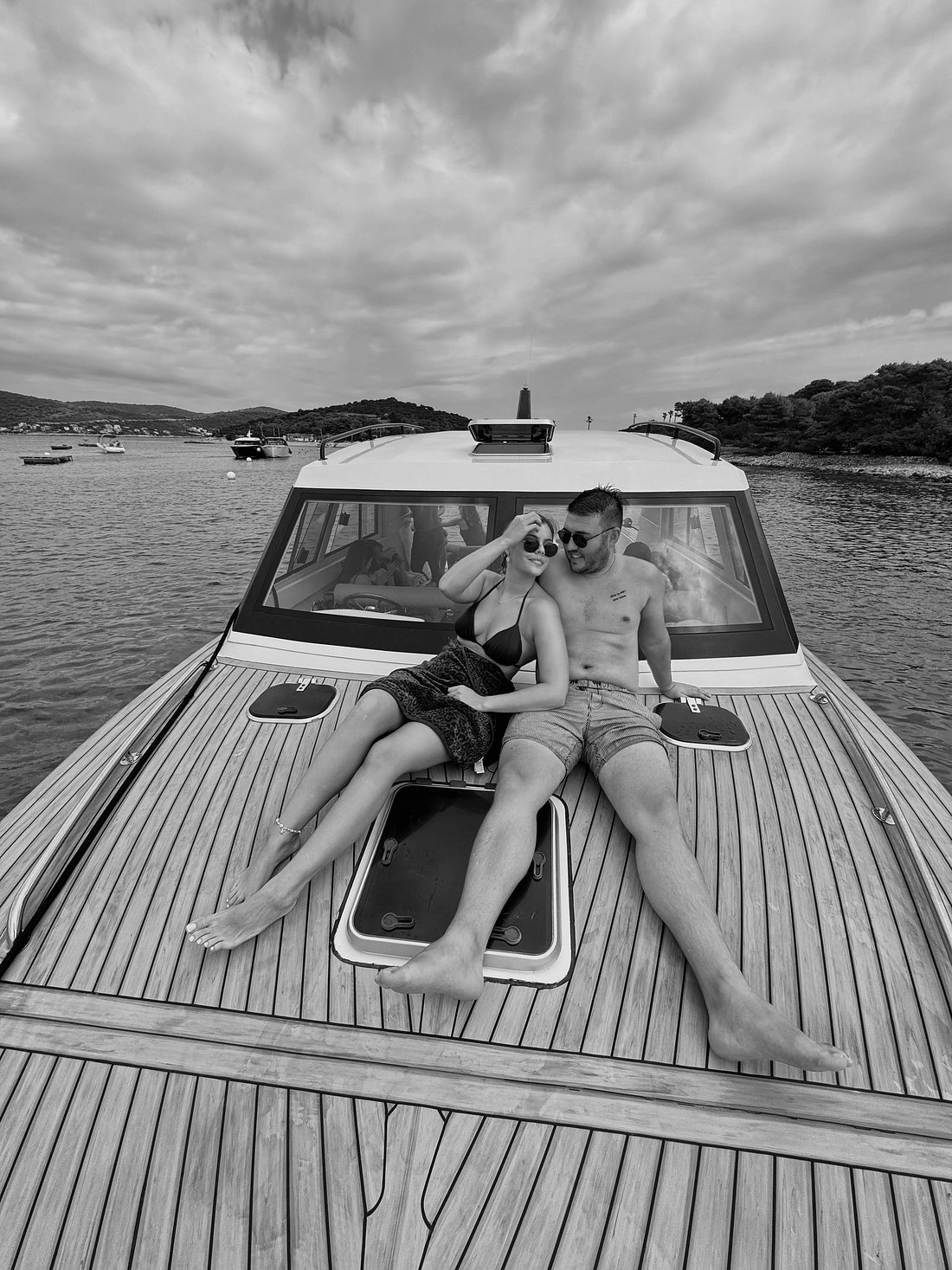 A couple relaxing on the bow of a boat, lying on the wooden deck while anchored in a calm bay