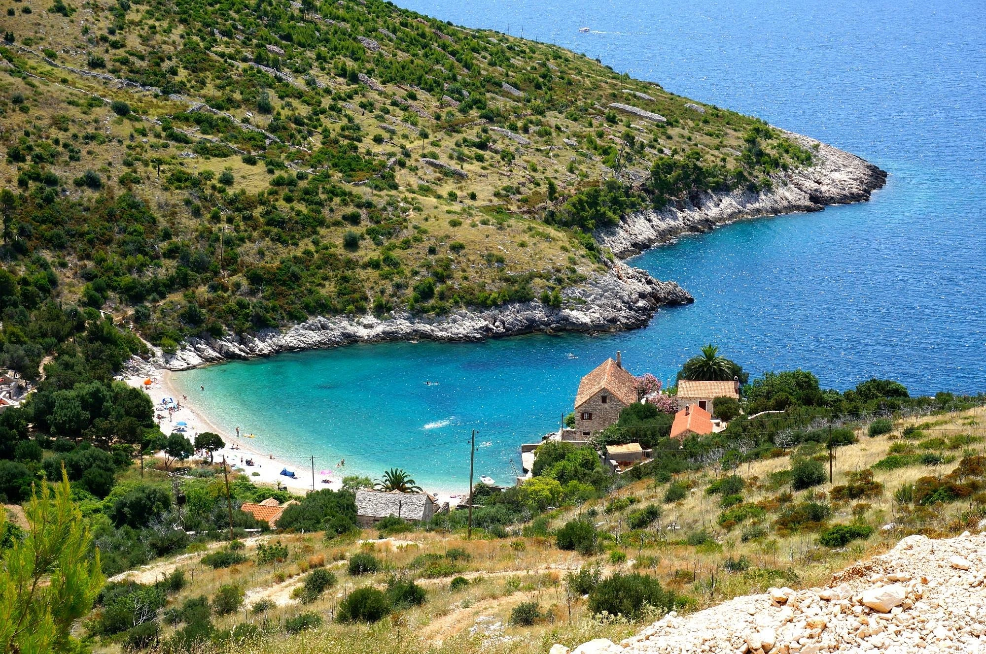 Scenic view of Dubovica Beach on Hvar, with turquoise water, a pebble shore, and traditional stone houses surrounded by greenery