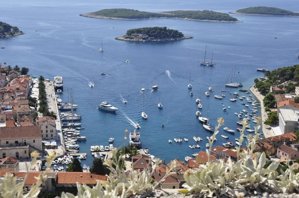 Panoramic view of Hvar town and its harbor from the Fortica fortress, showing red-roofed buildings, numerous boats in the turquoise bay, and small green islands in the background