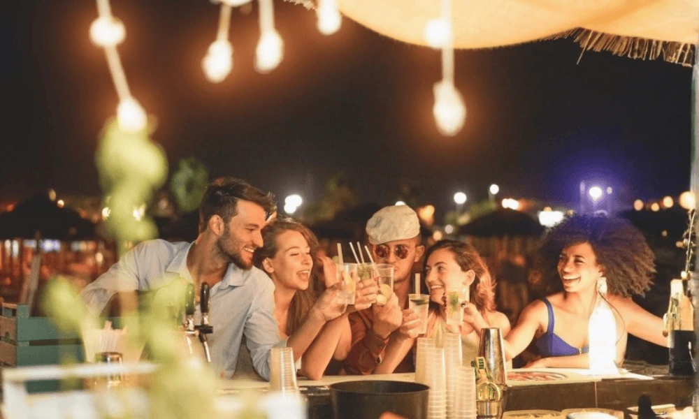 Grupa przyjaciół wspólnie delektuje się koktajlami w tętniącym życiem barze na plaży w Hvarze podczas letniego wieczoru.