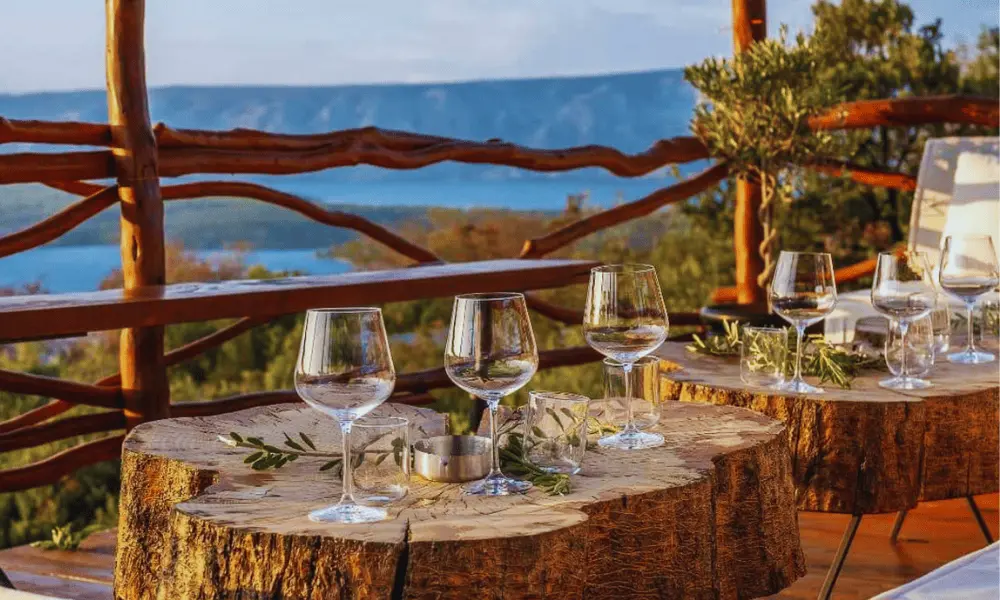 Rustykalny stół do degustacji win na świeżym powietrzu na wyspie Hvar, wykonany z naturalnego drewna, z widokiem na morze i okoliczne wzgórza o zachodzie słońca.