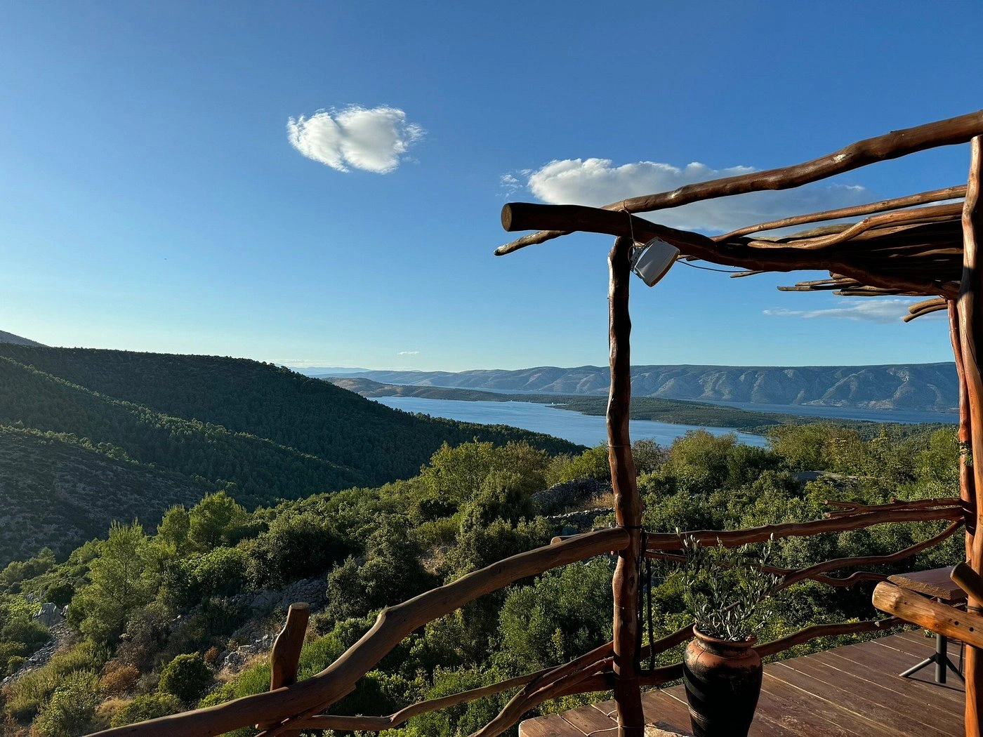 Scenic hilltop view overlooking lush green valleys and the blue Adriatic Sea, framed by a rustic wooden terrace with handcrafted beams and a potted plant