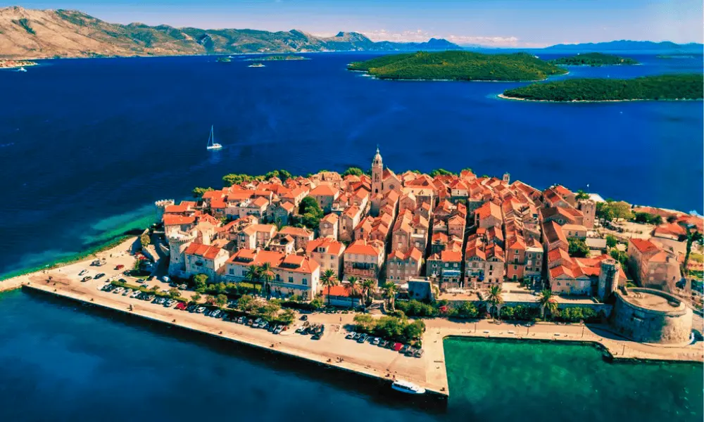 Widok z lotu ptaka na starówkę Korčuli, zabytkowy, otoczony murem półwysep z kamiennymi domami i pomarańczowymi dachami, otoczony Morzem Adriatyckim.