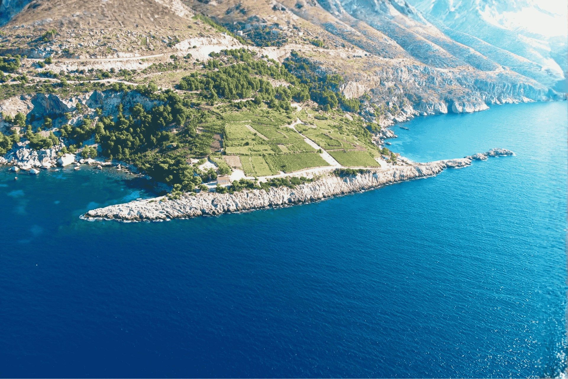 Aerial view of Zaraće on Hvar Island, showing dramatic rocky coastline, terraced greenery, and deep blue Adriatic waters.