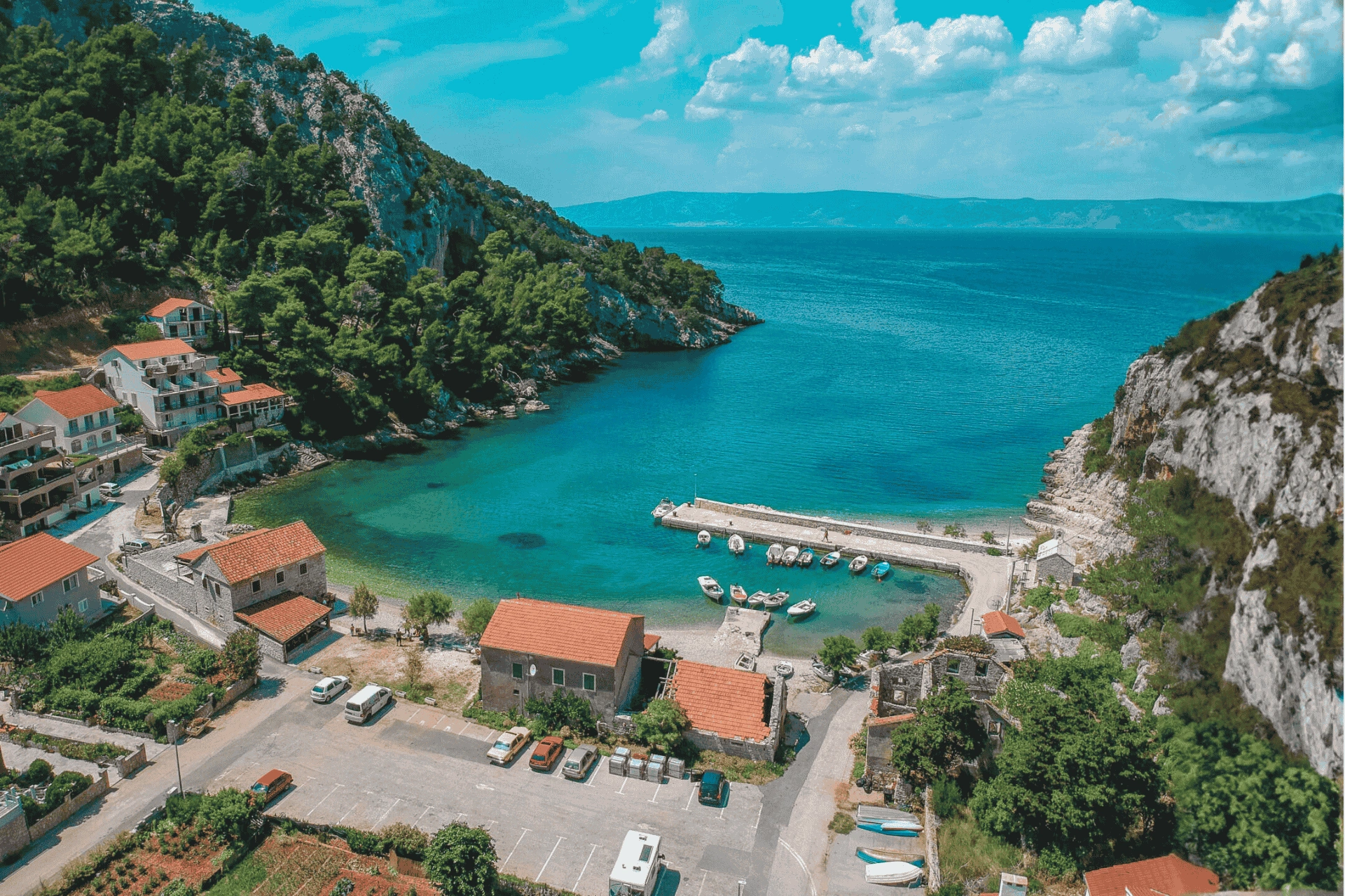Scenic aerial view of the charming bay in Zastražišće on Hvar Island, showing turquoise water, small boats, stone houses, and lush green hills.